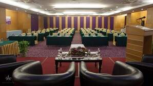 Un salón de conferencias con filas de mesas y sillas, un atril y suelo alfombrado.