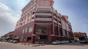 Un edificio de varios pisos con balcones, grandes ventanales y un estacionamiento al frente.