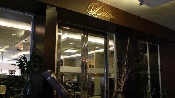 Entrada de hotel con puerta de cristal, un letrero sobre la puerta y plantas en macetas afuera.