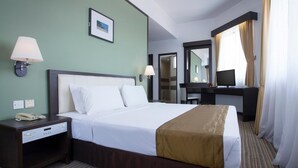 Una habitación de hotel con una cama grande, mesitas de noche, un escritorio, una silla, una lámpara, un espejo y una ventana con cortinas.