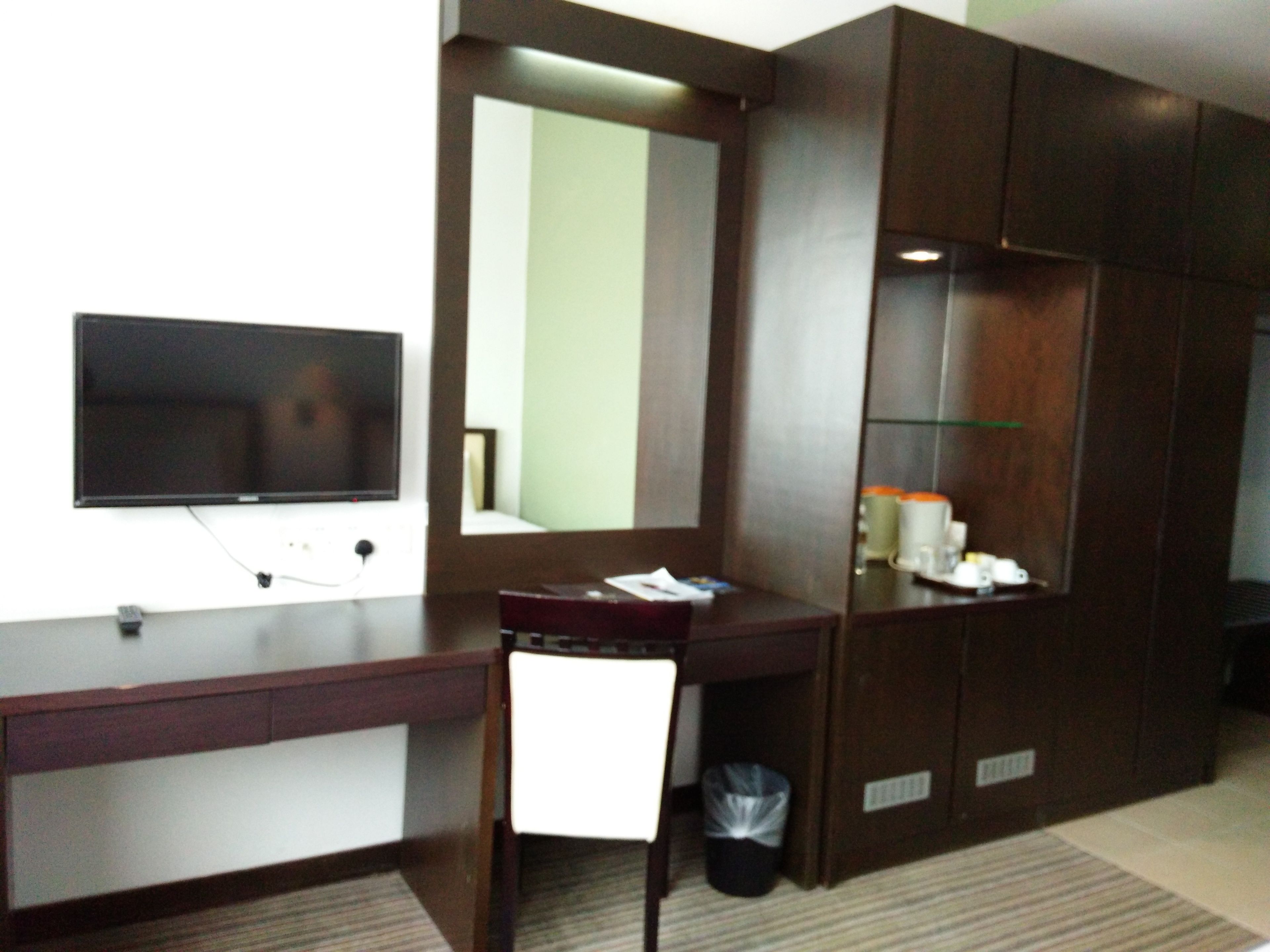 Een hotelkamer met een bureau, een televisie, een spiegel en een kledingkast.