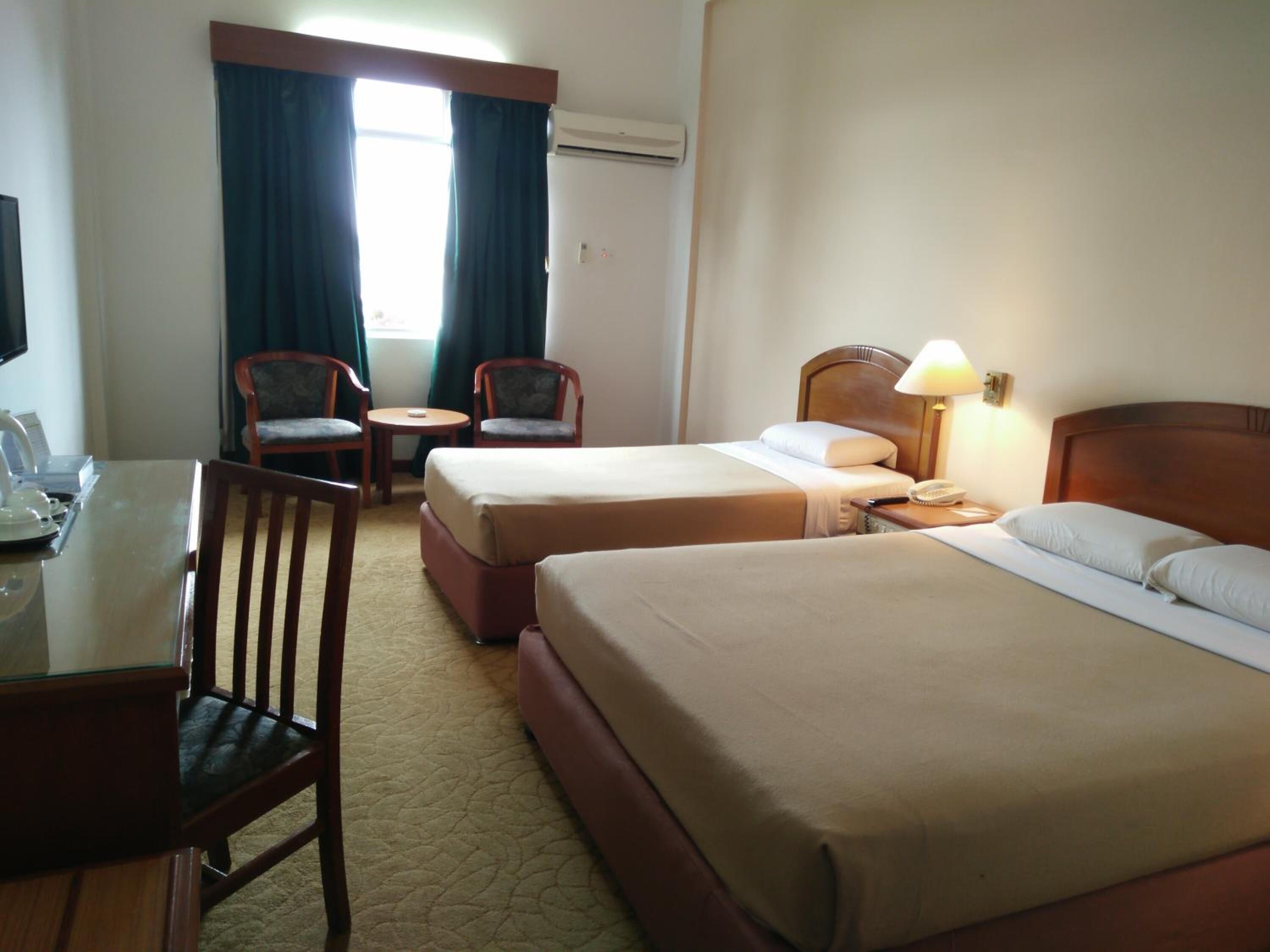 A hotel room with two beds, a desk, a chair, a small table, and a lamp.