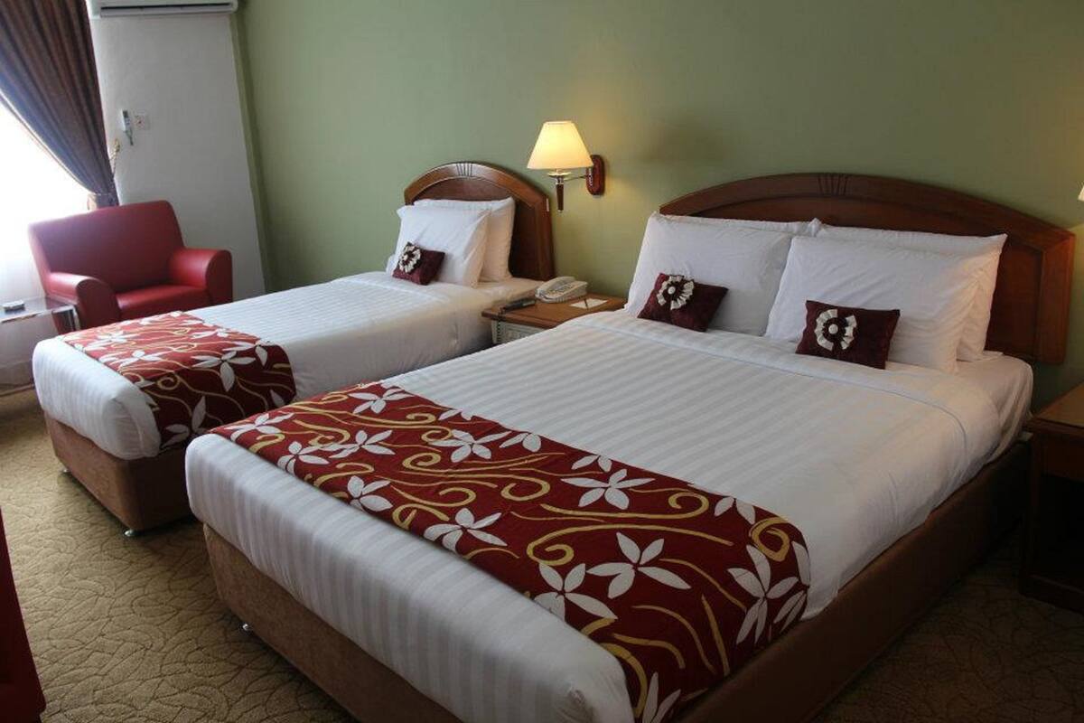 Quarto de hotel com duas camas, uma cadeira vermelha, um abajur e um telefone.