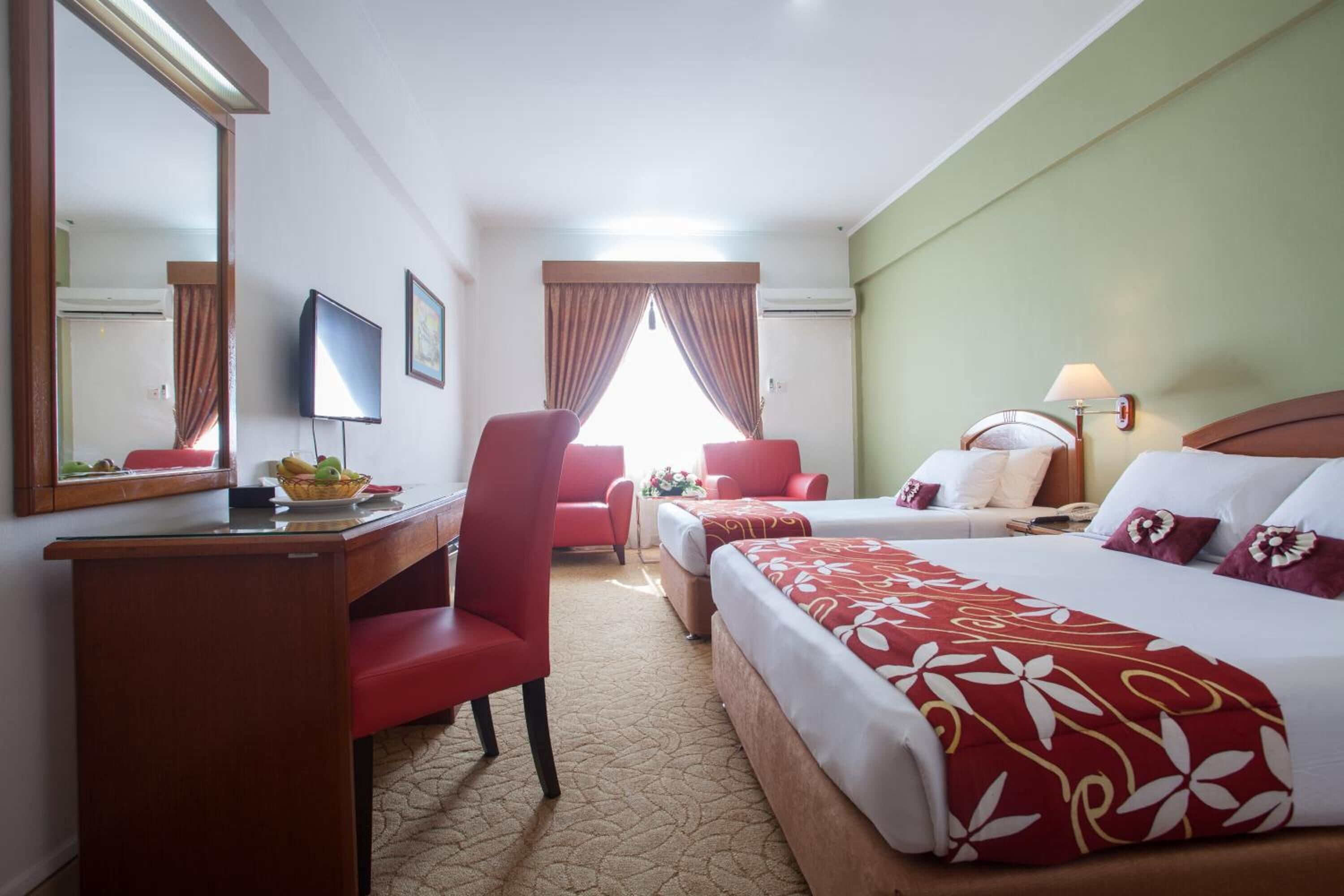 A hotel room with a bed, a desk, a chair, a television, and a window with curtains.