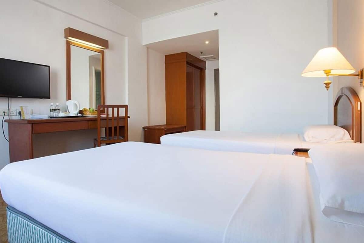 A hotel room with two beds, a desk with a chair, a television, and a lamp.