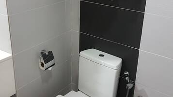 Ein modernes Badezimmer mit Toilette, Handtuchhalter mit gefalteten Handtüchern, Toilettenpapierhalter und Duschkopf.
