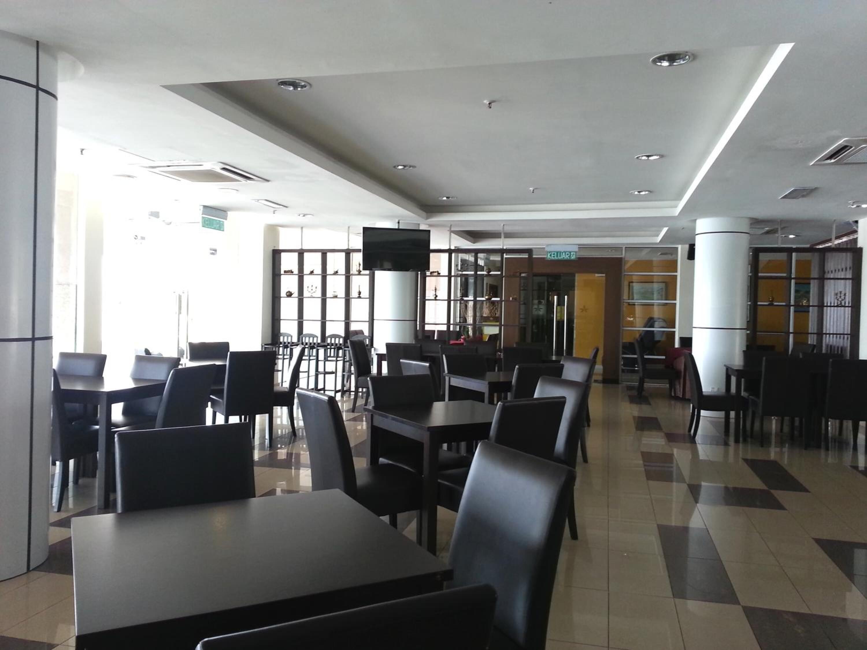Un'ampia sala da pranzo interna con diversi tavoli e sedie, un grande schermo a parete e una vista libera sull'ingresso.