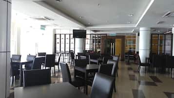 Un'ampia sala da pranzo interna con diversi tavoli e sedie, un grande schermo a parete e una vista libera sull'ingresso.