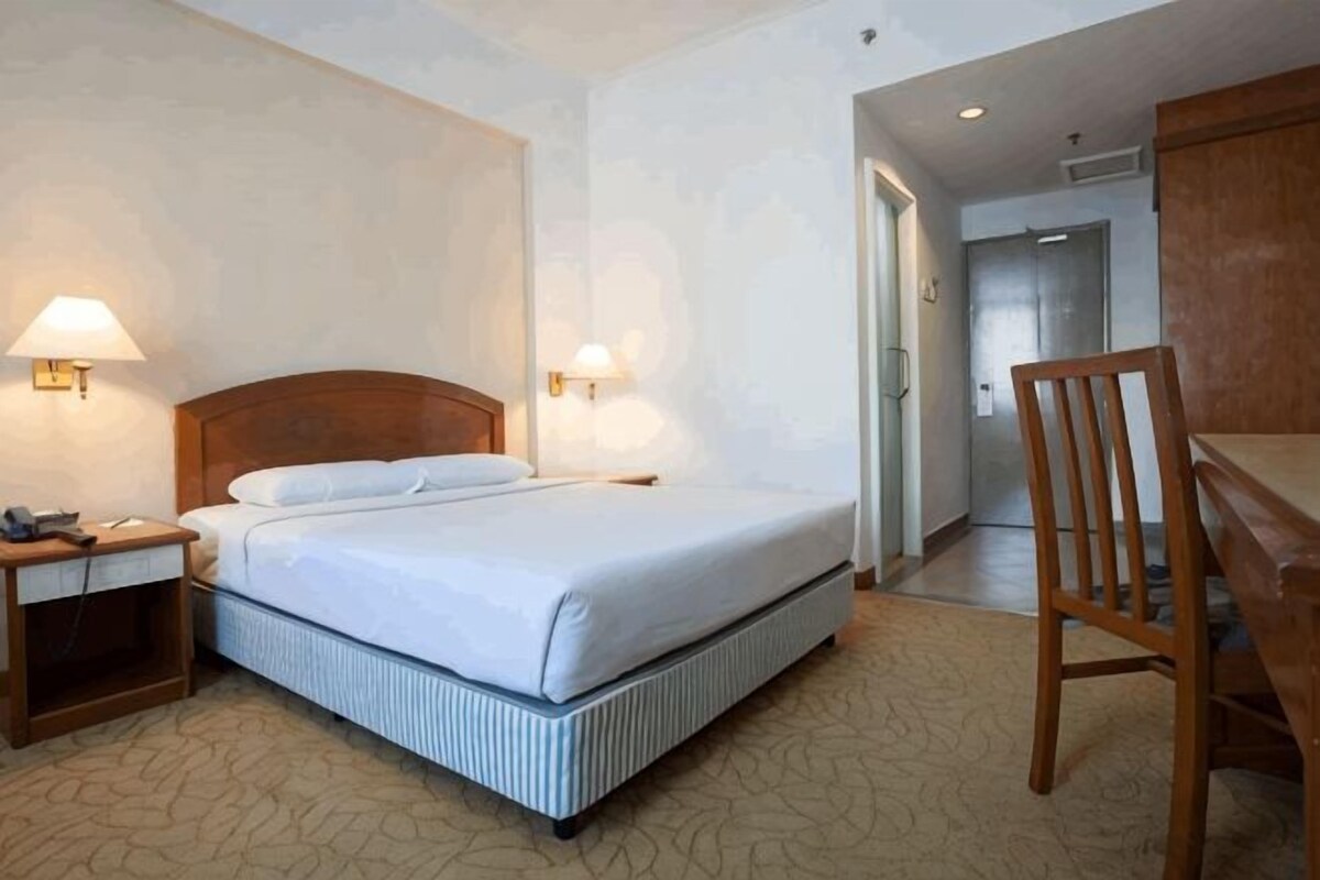 A hotel room with a bed, bedside lamps, a desk, and a chair.