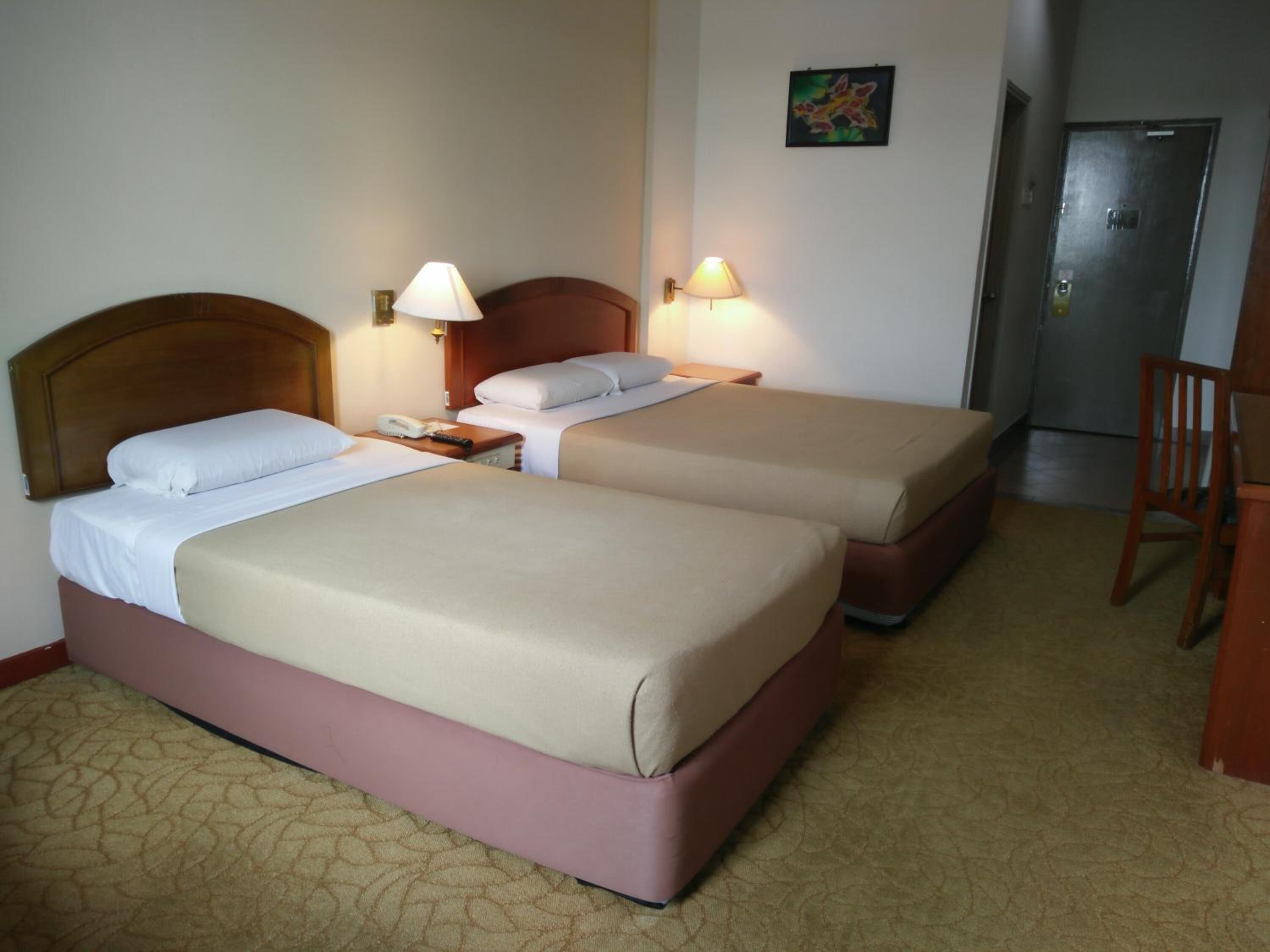 A hotel room with two beds, a desk, a chair, and a door.