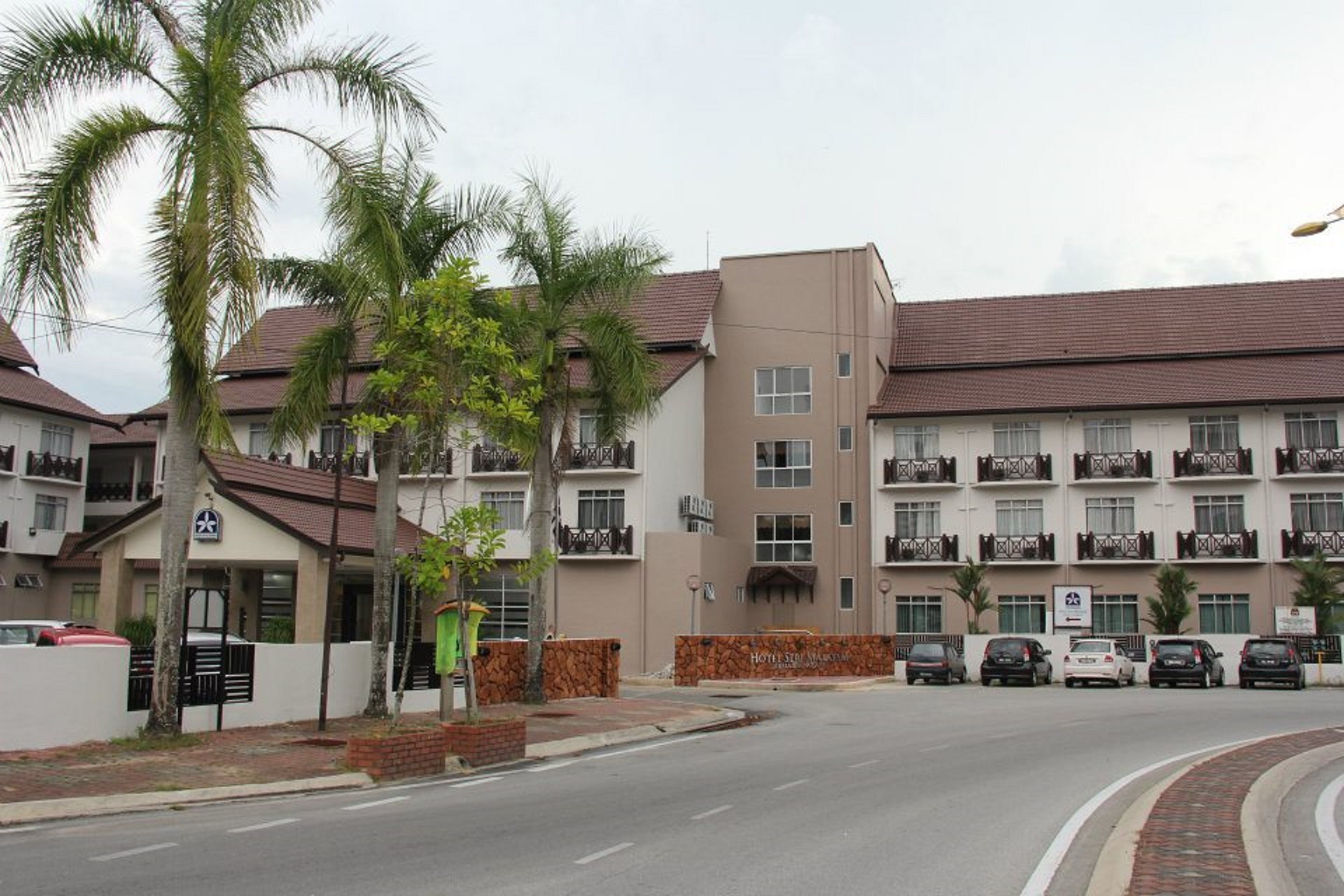 A multi-story hotel with balconies, a parking area, and palm trees.