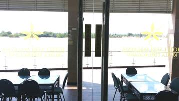 A restaurant with outdoor seating overlooking a body of water, featuring a logo and text on the glass doors.