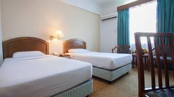 Quarto de hotel com duas camas, uma escrivaninha, uma cadeira e uma janela com cortinas.