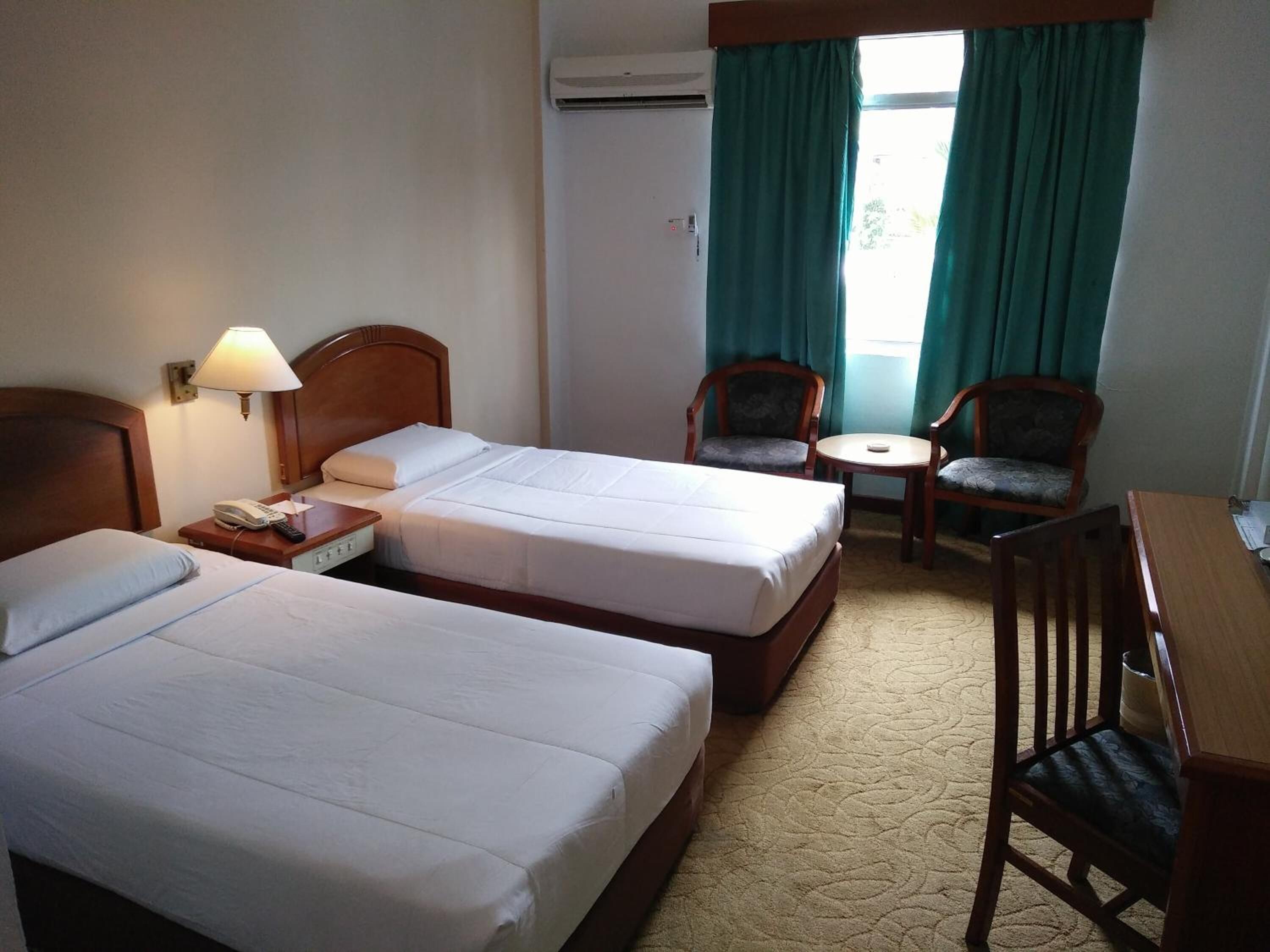 Habitación de hotel con dos camas, un escritorio, dos sillas, una lámpara y un equipo de aire acondicionado.