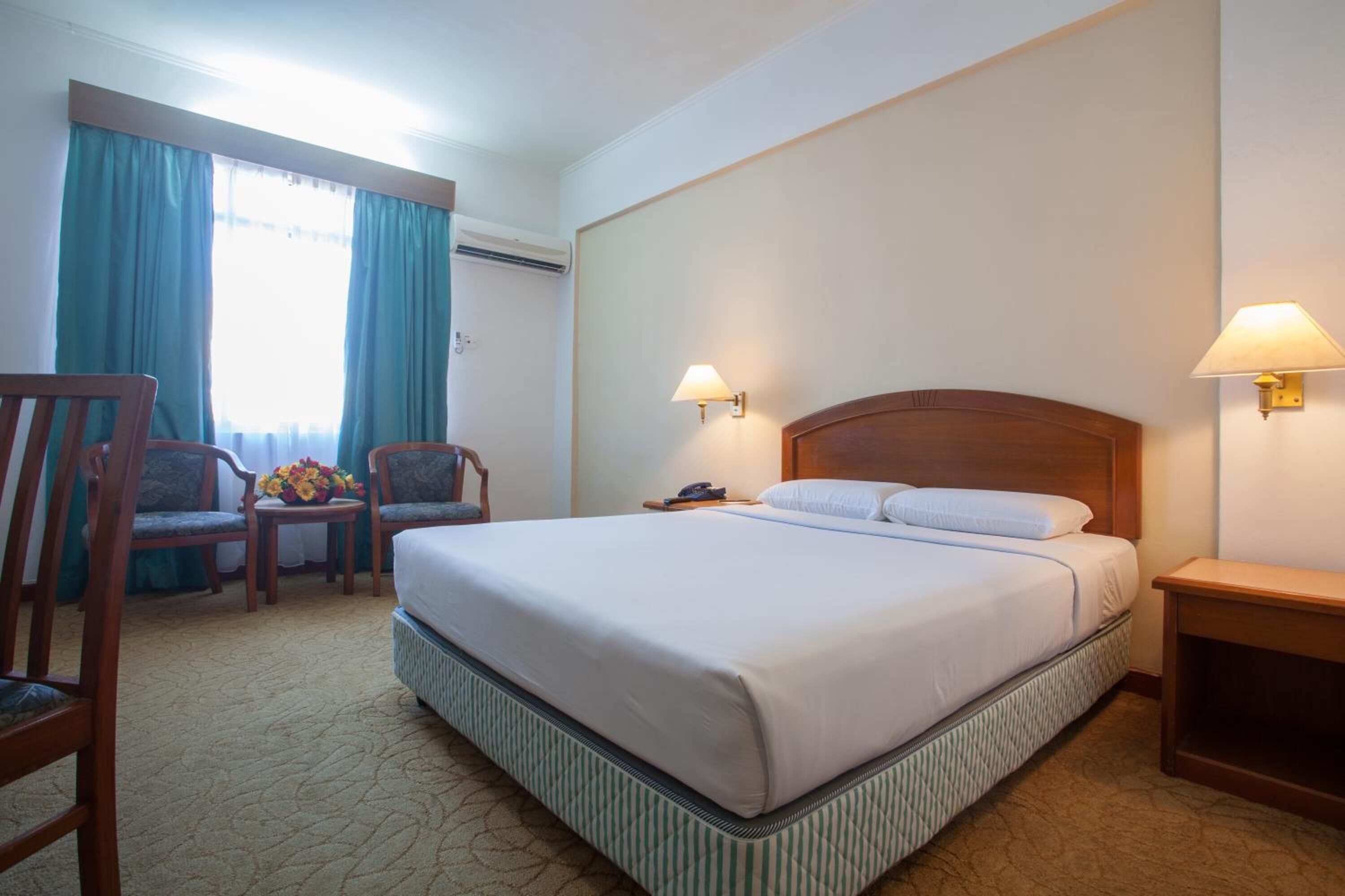 A hotel room with a large bed, two chairs, a small table with a vase of flowers, and a nightstand with a lamp.