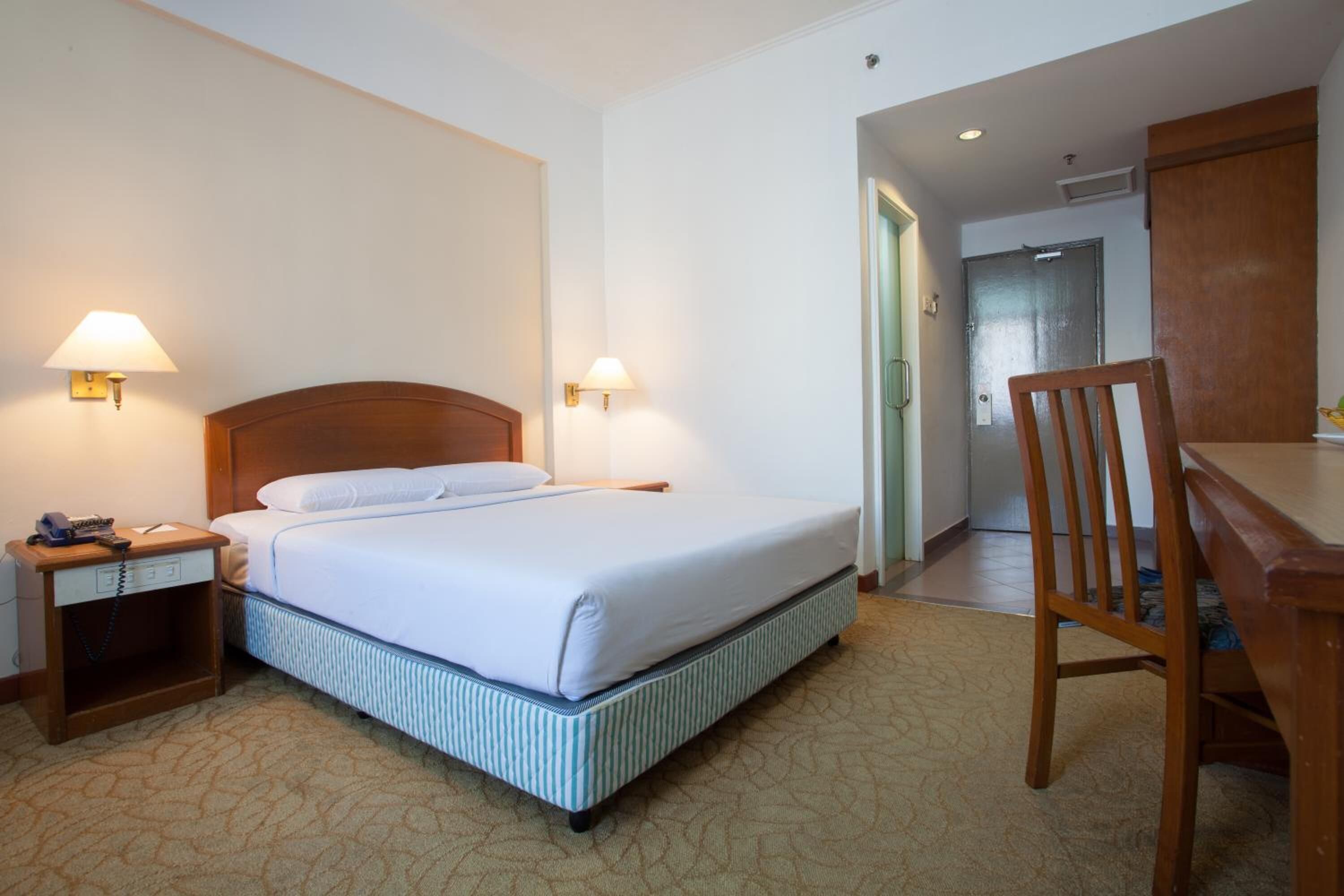 Ett hotellrum med en säng, sänglampor, ett skrivbord och en stol.