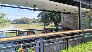 An outdoor seating area with tables and chairs, a view of a lake, and a brick wall with signs. - Hotel Seri Malaysia Kulim (Kulim)