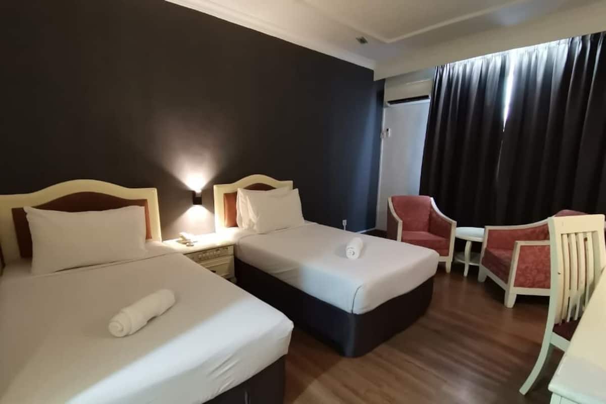 Habitación de hotel con dos camas, un escritorio, una silla y un ventanal con cortinas.