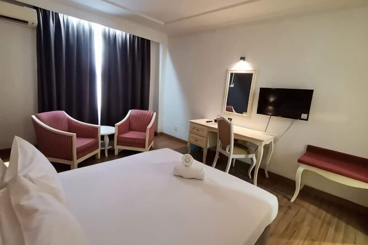 Habitación de hotel con cama, dos sillas rojas, escritorio, televisor y ventana con cortinas.