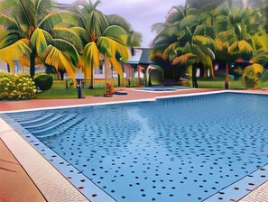Una piscina con superficie de agua azul cristalina, rodeada de palmeras y un césped bien cuidado.
