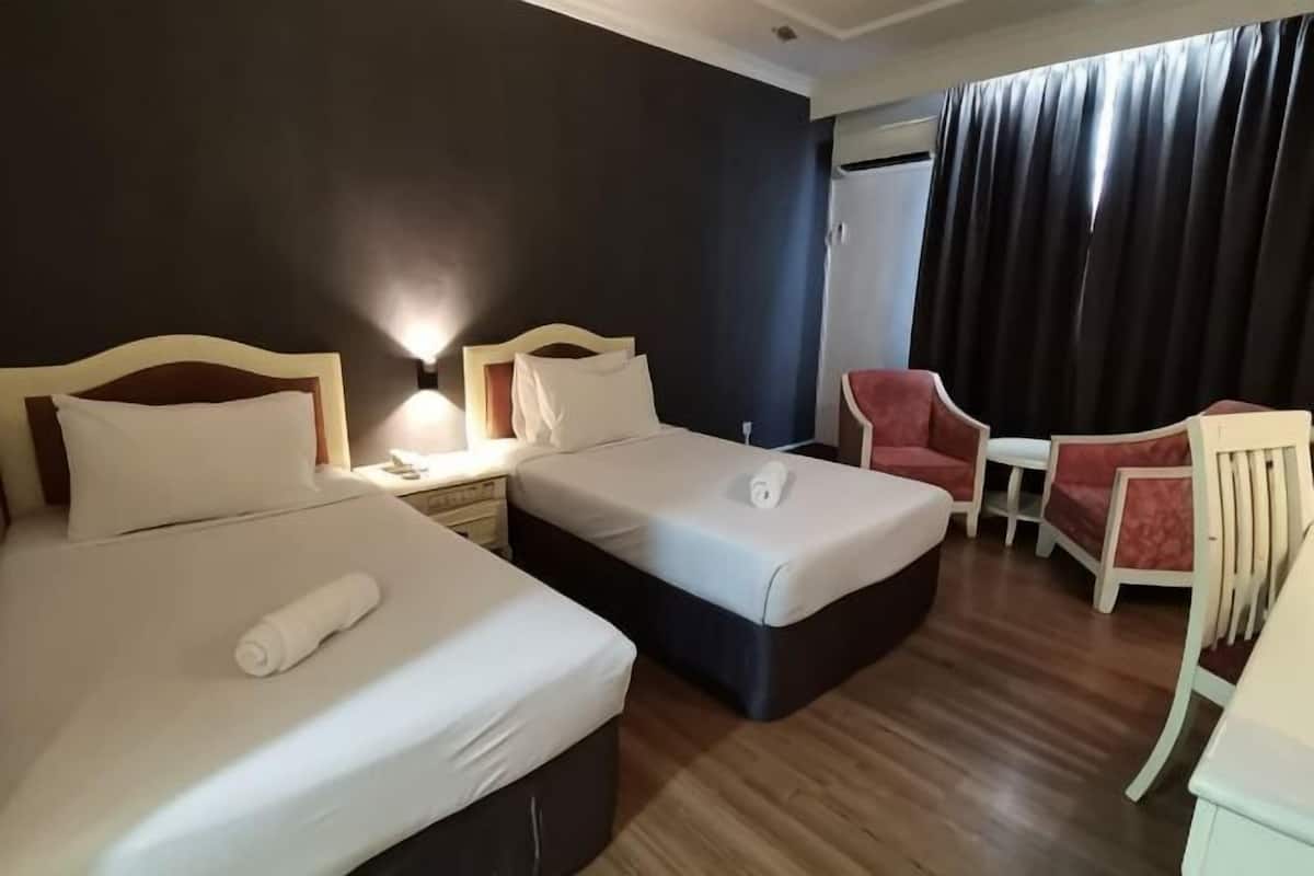Habitación de hotel con dos camas, un escritorio, una silla y una ventana con cortinas.