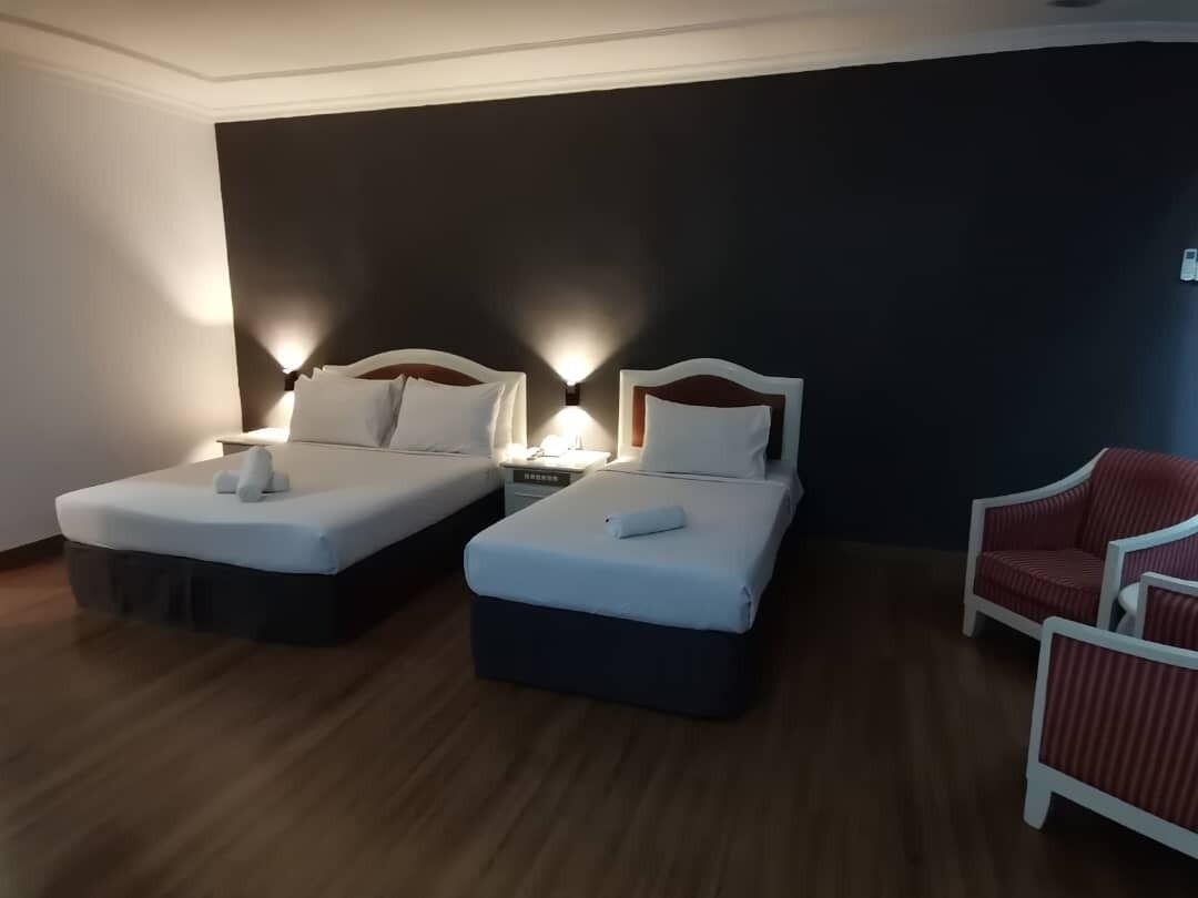 A hotel room with two beds, a red chair, and a nightstand with a lamp.