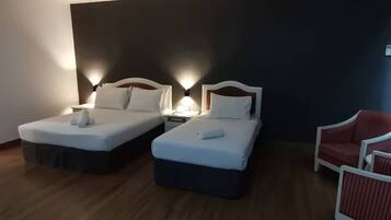 A hotel room with two beds, a red chair, and a nightstand with a lamp.