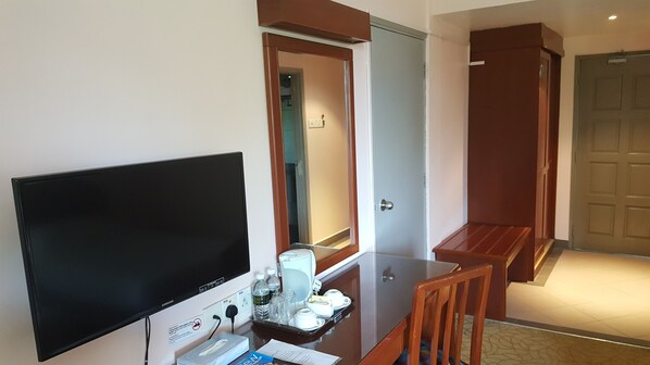 A hotel room with a flat-screen TV, a small table with a tray of toiletries, a wooden chair, and a door leading to another room. - Hotel Seri Malaysia Marang (Marang)