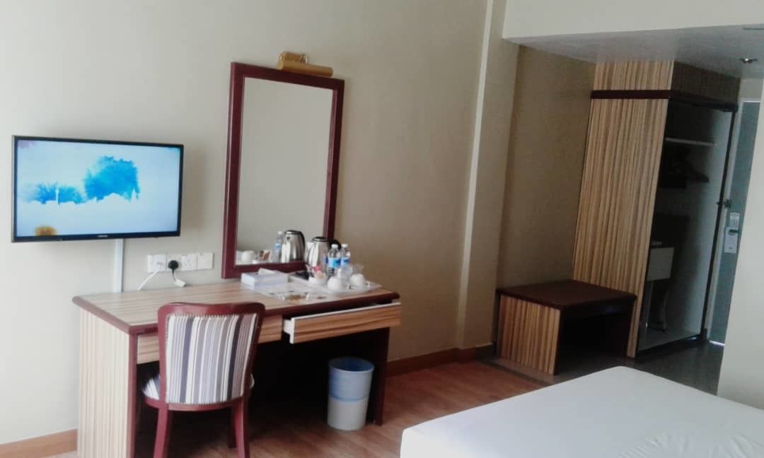 Una habitación de hotel con cama, escritorio, silla, espejo, televisor y armario.