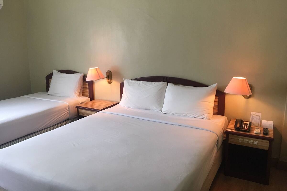 A hotel room with two single beds, each with a bedside table, lamp, and a telephone.