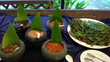 Una mesa con cuencos de piedra que contienen diferentes platos, un plato de verduras verdes y una cuchara y unas pinzas sobre un mantel azul.