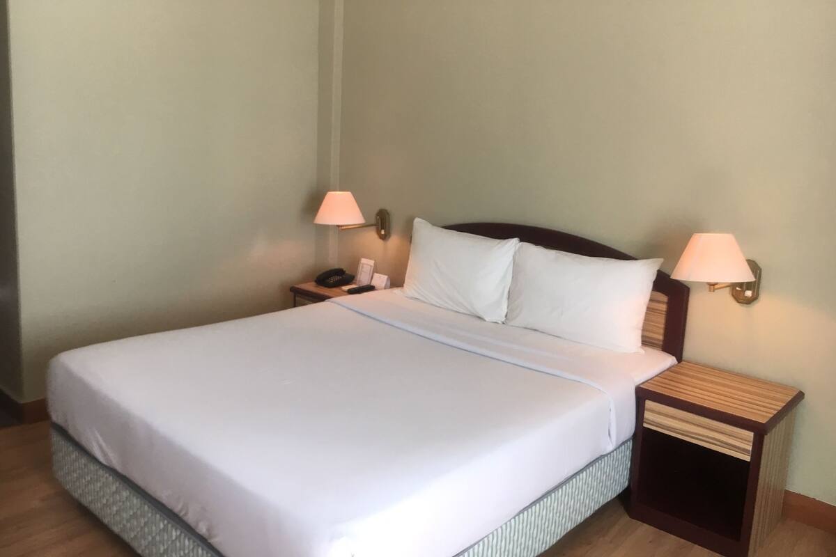 A neatly made bed with white linens, two bedside lamps, a nightstand with a phone and a lamp, and a wooden floor.