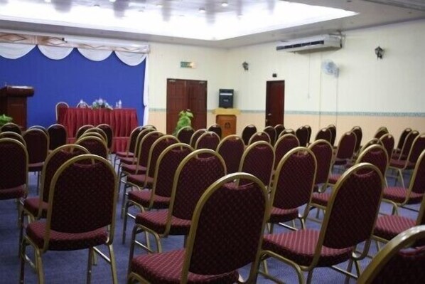 Un salón de conferencias con filas de sillas, un atril y un telón de fondo azul.