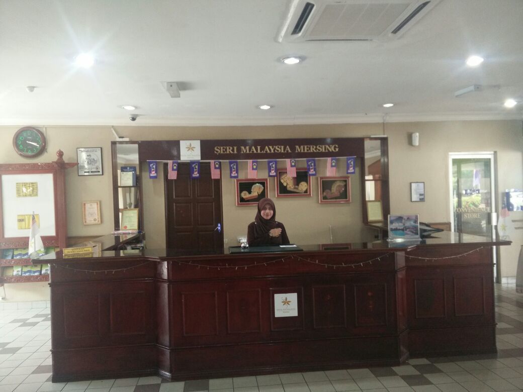 A reception desk with a sign reading "SERI MALAYSIA MERSING" and a clock on the wall.
