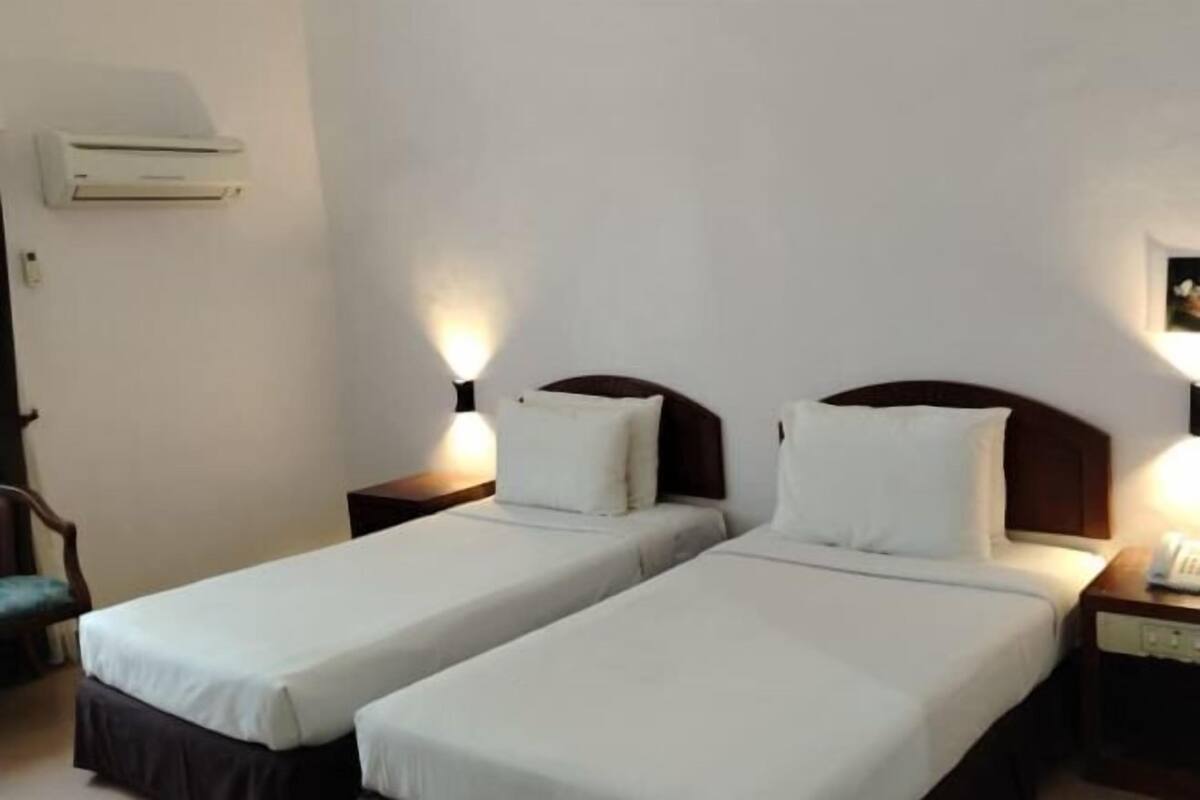 Habitación de hotel con dos camas individuales, mesitas de noche, aire acondicionado en la pared y una silla.