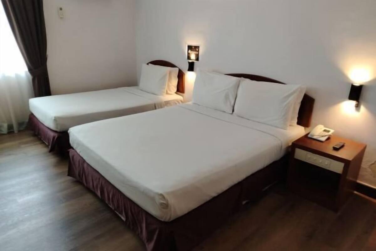 Una habitación de hotel con dos camas, una mesita de noche con teléfono e iluminación en la pared.