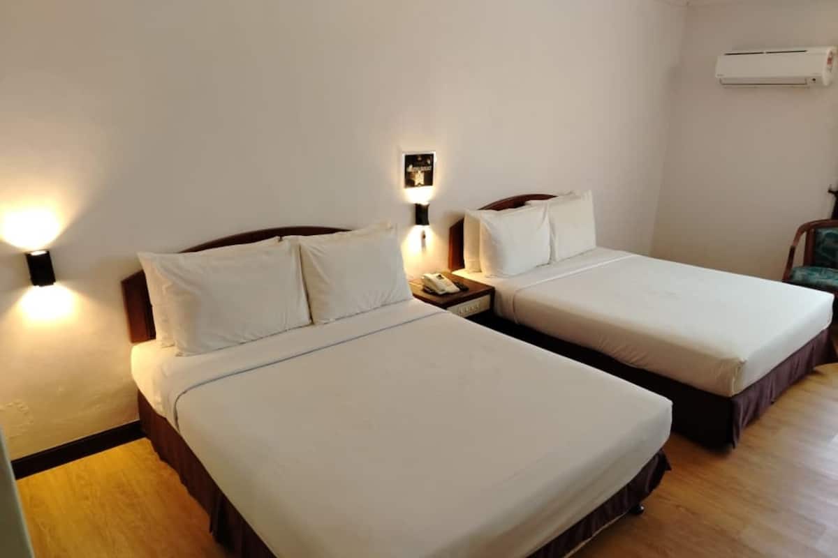 Una habitación de hotel con dos camas individuales, una mesita de noche con teléfono, aire acondicionado instalado en la pared y suelo de madera.