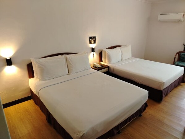 Ein Hotelzimmer mit zwei Einzelbetten, einem Nachttisch mit Telefon, einer Wand-Klimaanlage und Holzboden.