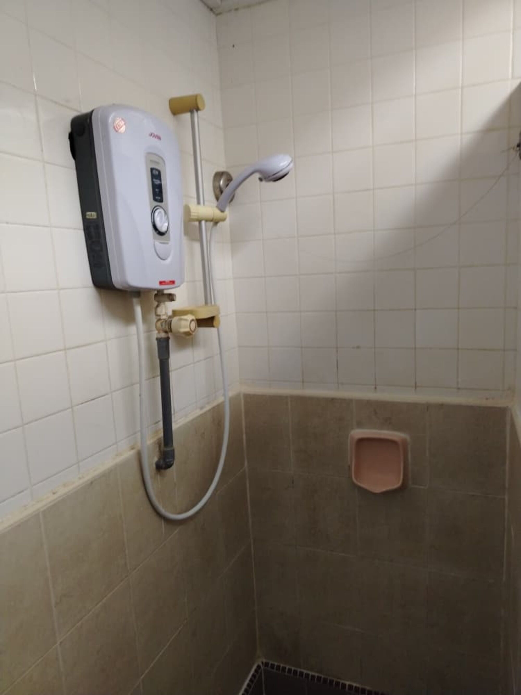 Piccola zona doccia con piastrelle, soffione a mano, pannello comandi a parete e scarico a pavimento.