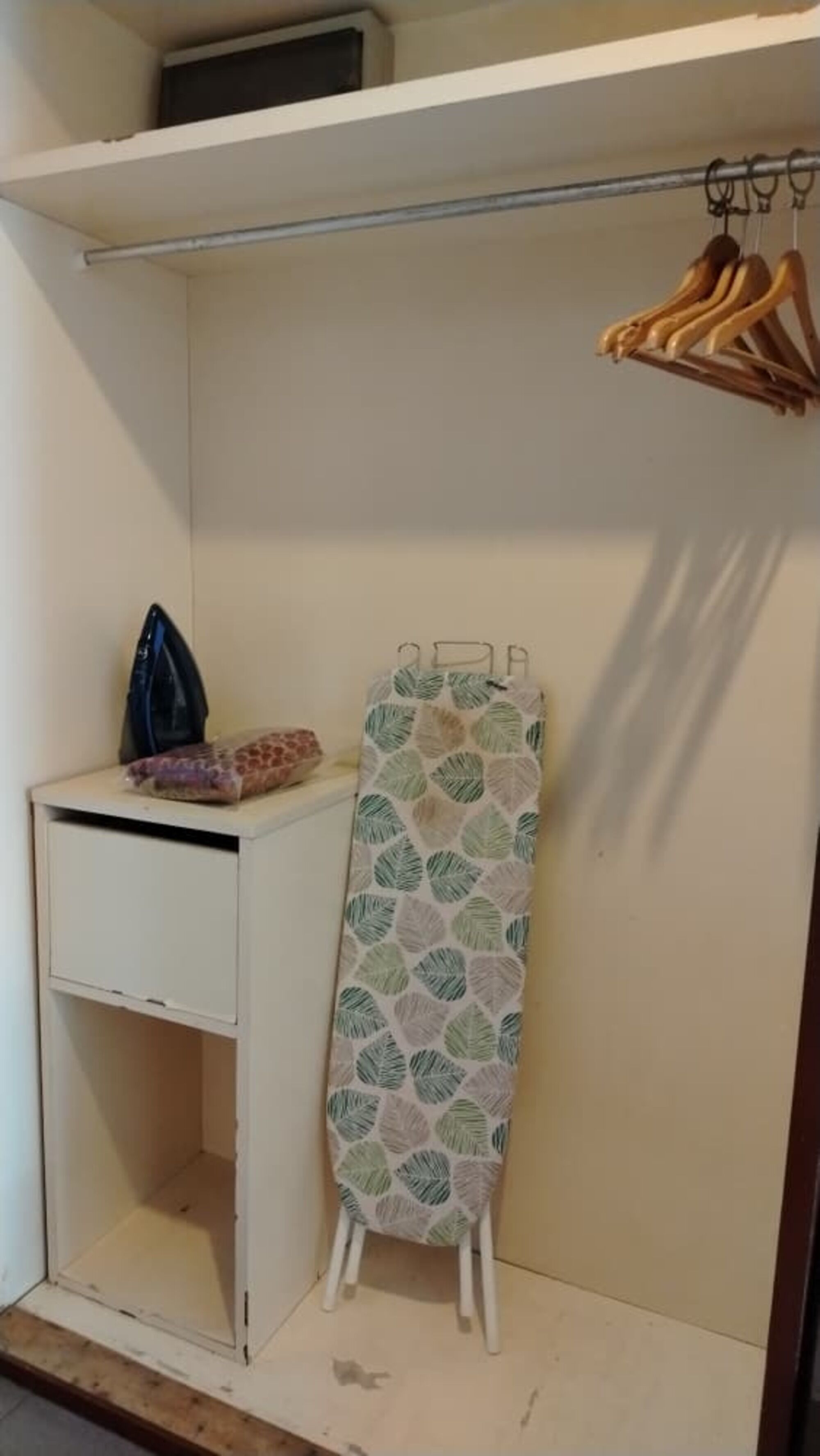 Un armario pequeño y blanco con una percha y una tabla de planchar.