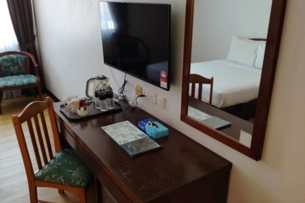 Une chambre d’hôtel avec un bureau en bois, une télévision, un lit et un miroir qui reflète la pièce.