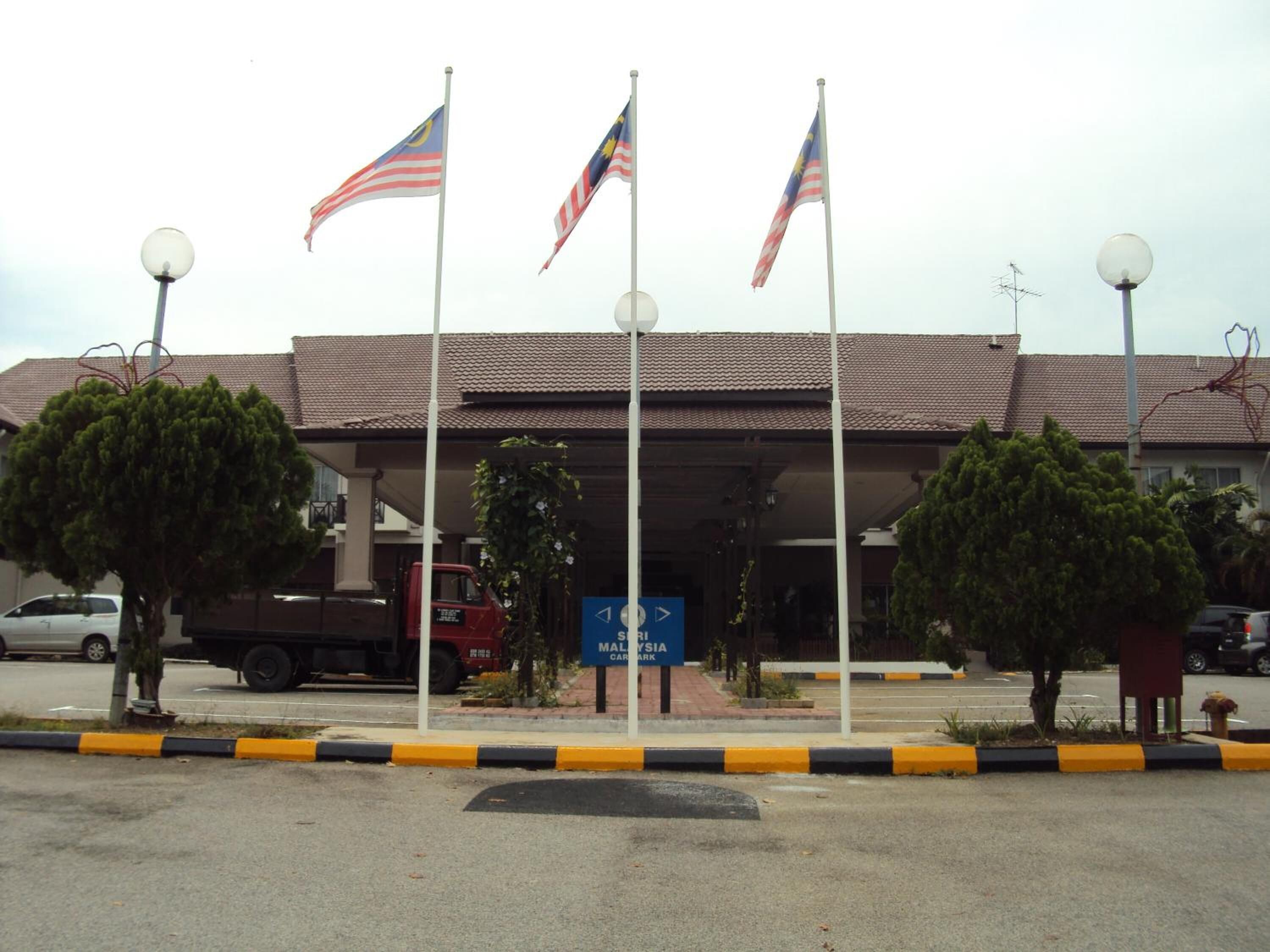 A parking area with multiple flags, a sign for Malaysia Car Park, and a building with a tiled roof.
