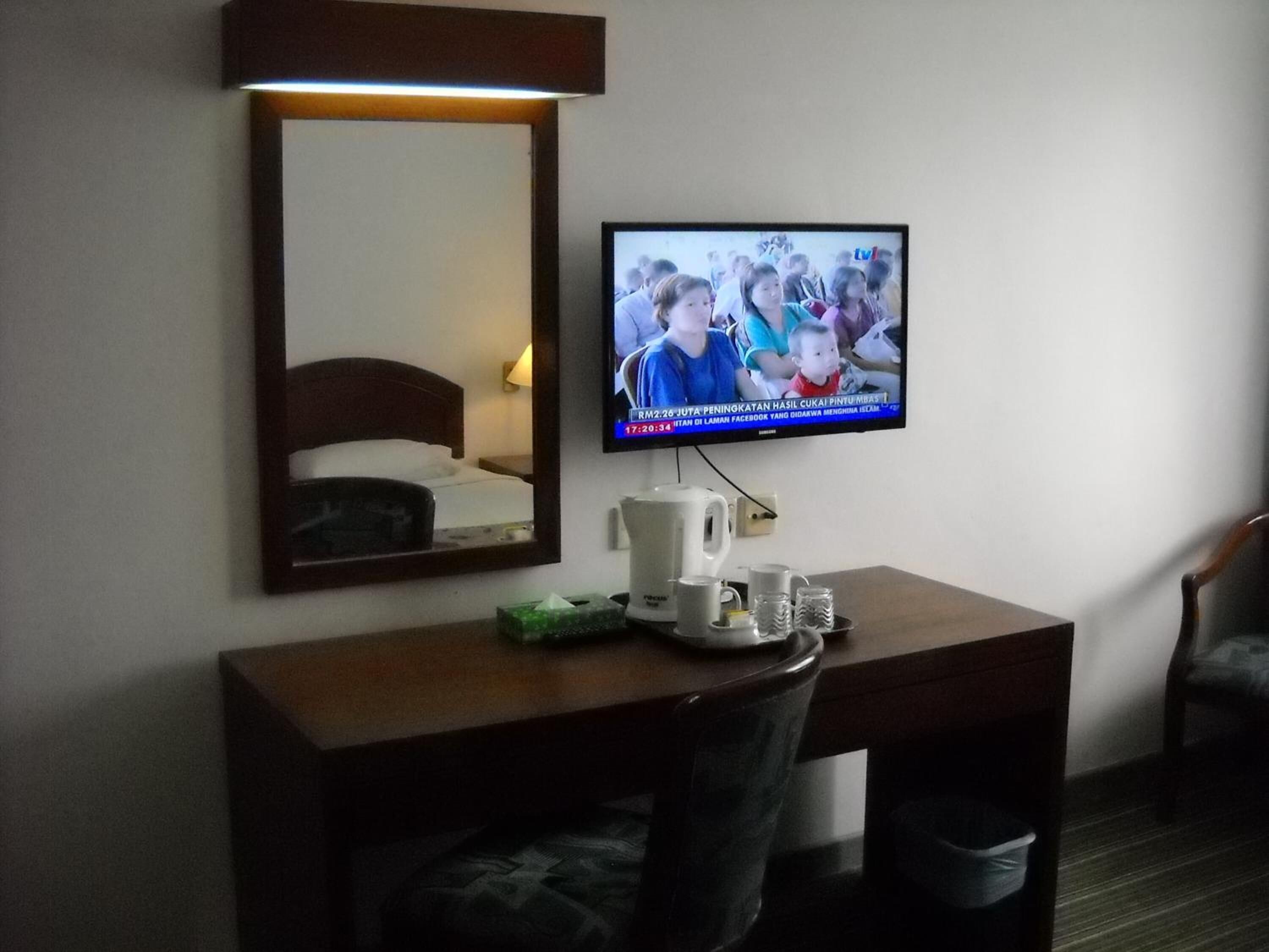 A hotel room with a desk, a television mounted on the wall, a bed with a headboard, and a chair.