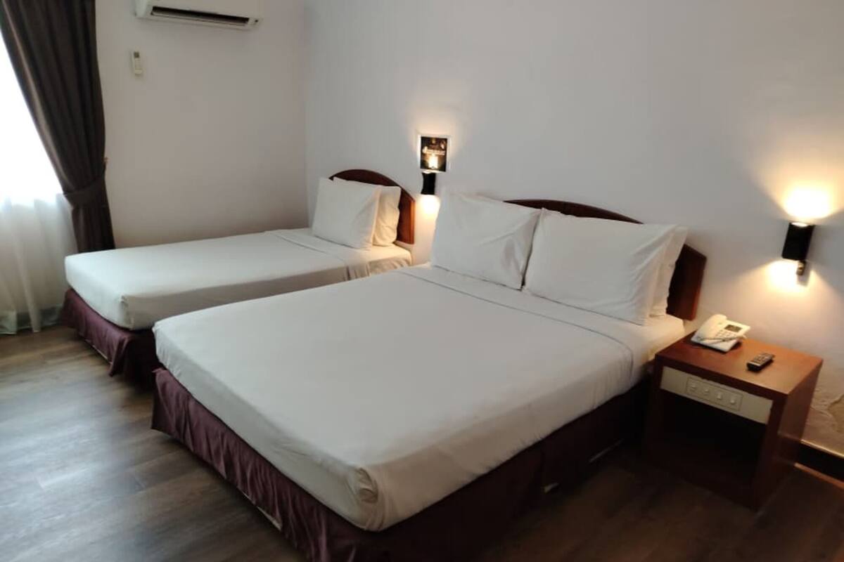 Habitación de hotel con dos camas, una mesita de noche con teléfono y control remoto, y una lámpara de pared.