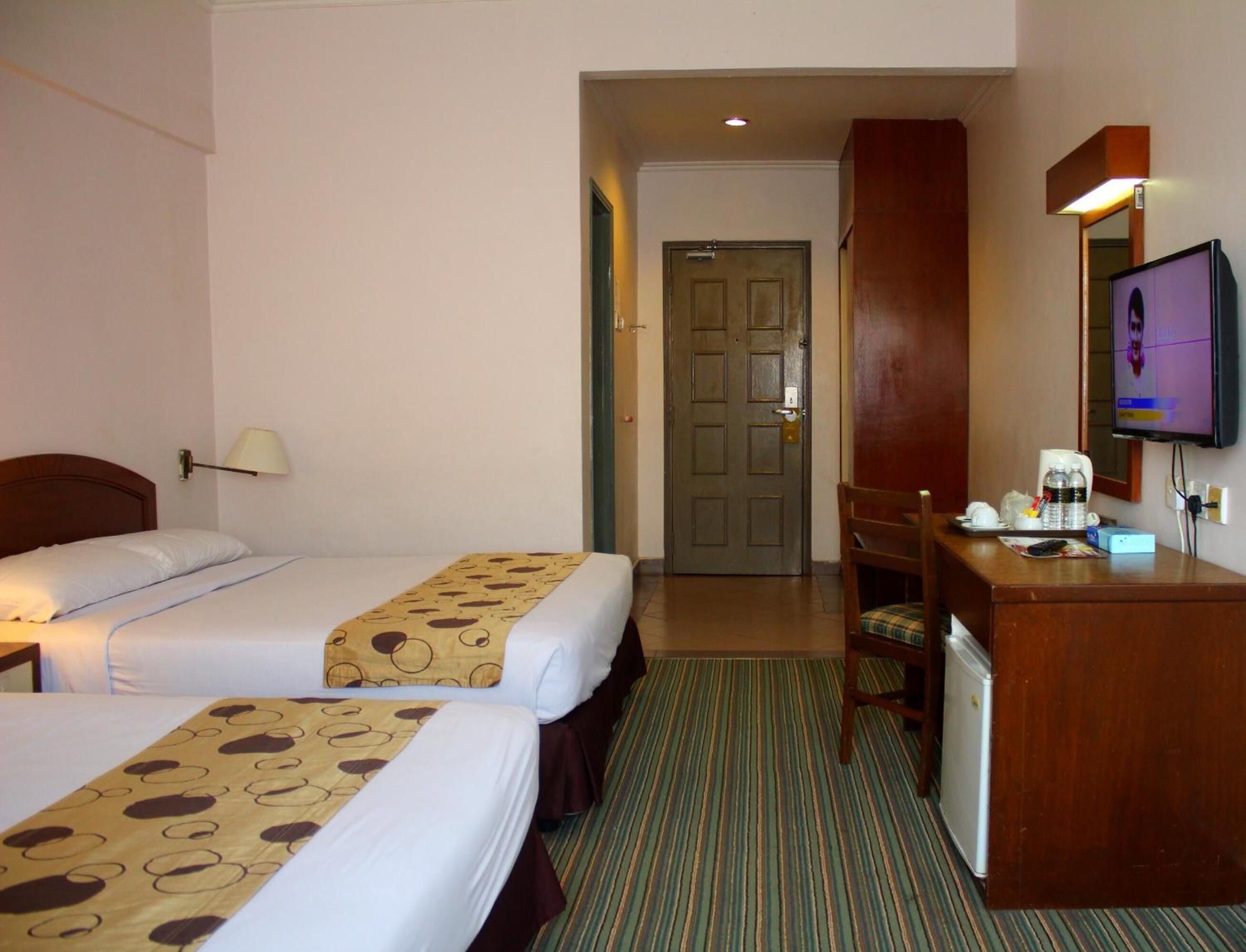 A hotel room with two beds, a desk, a chair, a television, and a door leading to another room.