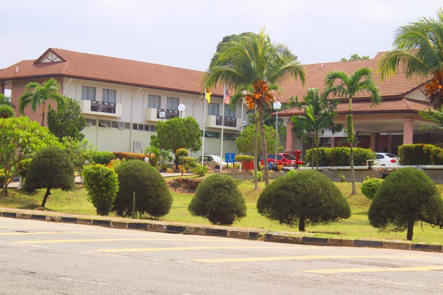 A hotel with a red-tiled roof, multiple balconies, and a well-maintained garden with palm trees and shrubs.