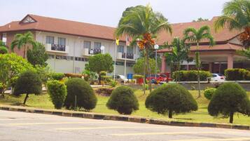 A hotel with a red-tiled roof, multiple balconies, and a well-maintained garden with palm trees and shrubs.