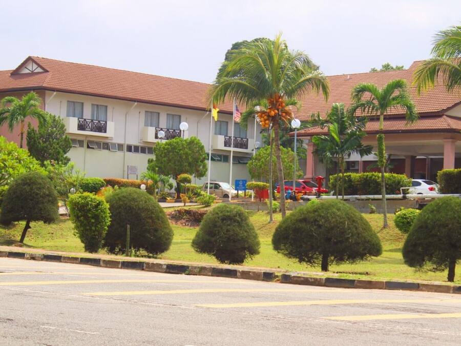 A hotel with a red-tiled roof, multiple balconies, and a well-maintained garden with palm trees and shrubs.