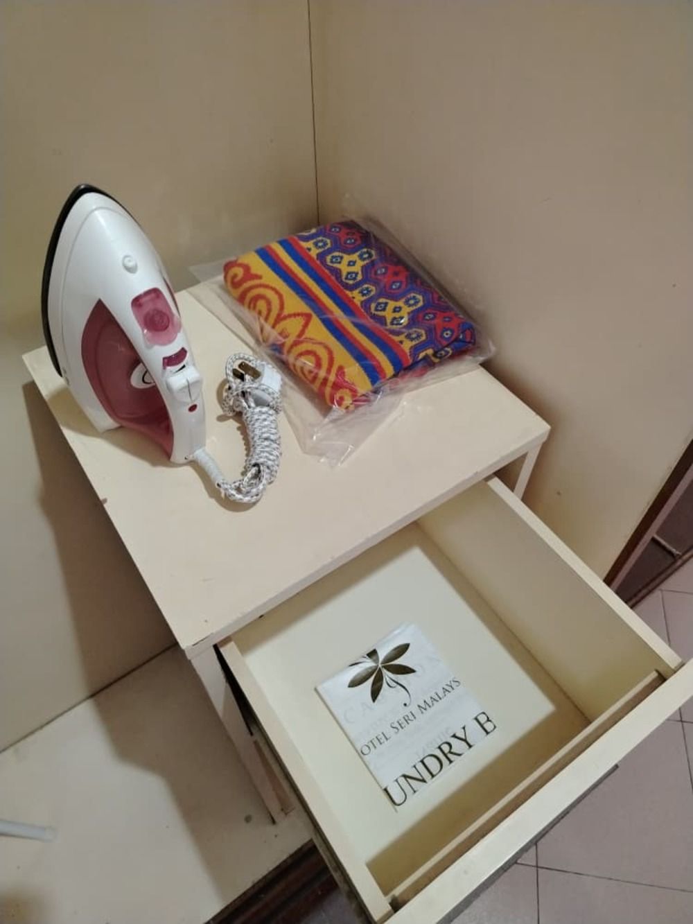 Una plancha blanca, un paño estampado y un cajón con un cartel que dice 