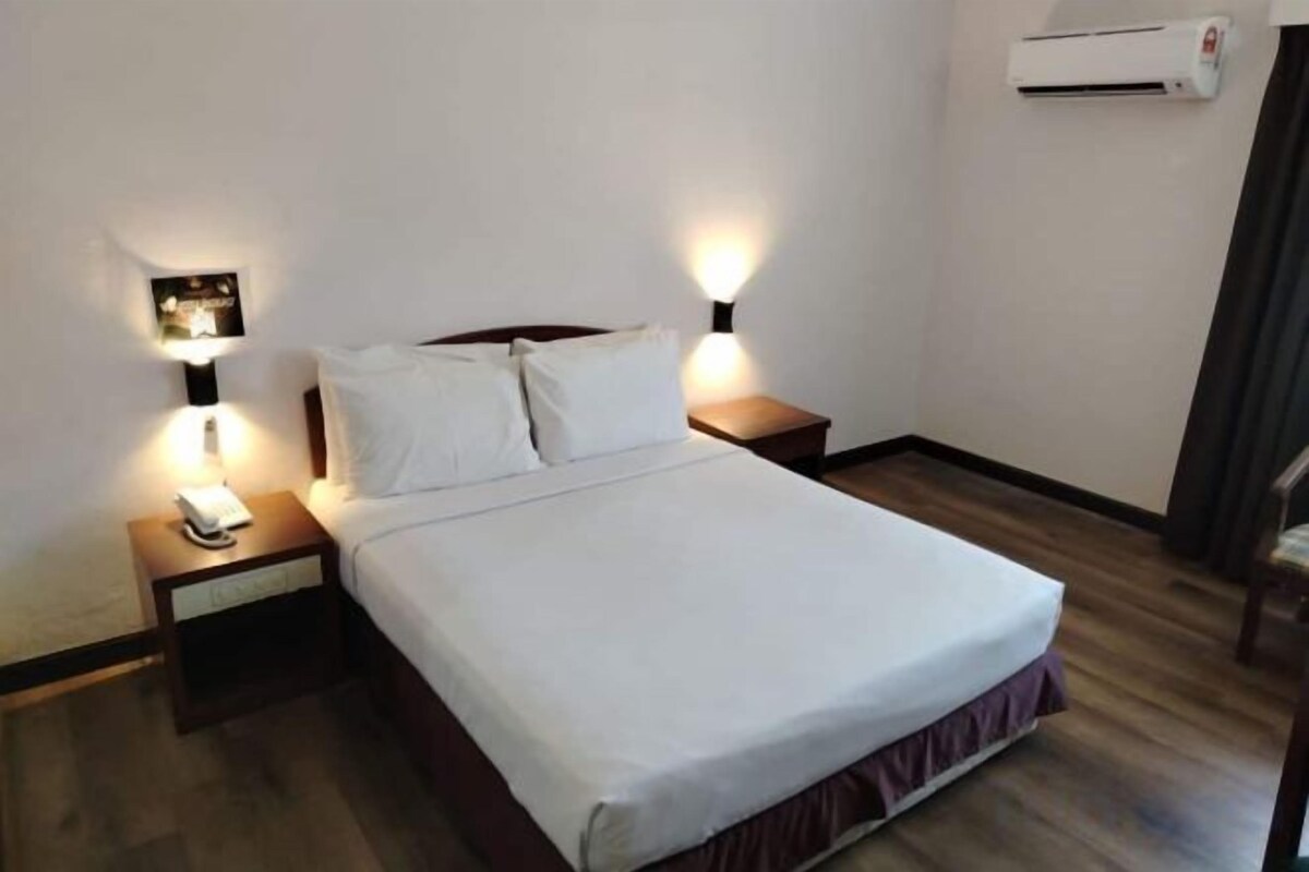 Una habitación de hotel con cama, lámparas de noche, mesita de noche y aire acondicionado.